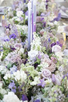 the table is set with purple and white flowers, candles, and silverware on it