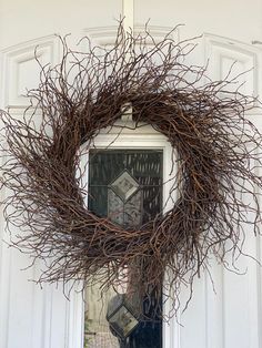 a twig wreath hanging on the front door of a white house with a window