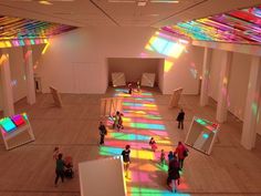 people are walking around in an art museum with colorful lights on the walls and floors