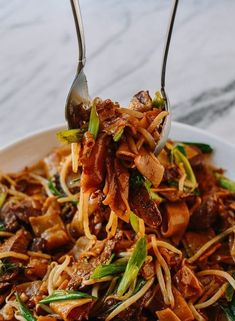 a plate with noodles, meat and vegetables being held up by two tongs over it