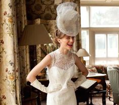 a woman wearing a white dress and hat in a living room with floral wallpaper