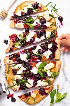 four flatbread pizzas topped with blueberries, cheese and herbs on a marble surface