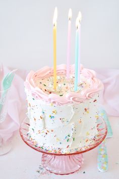 a birthday cake with white frosting and pink icing has five lit candles on it