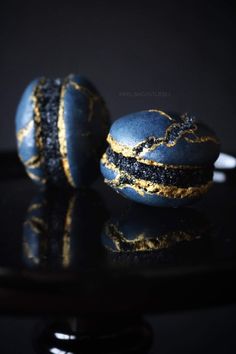 two blue and gold macaroons sitting on top of a black table next to each other