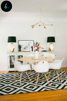 a dining room with white chairs and a black and white rug in front of the table