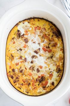 a casserole dish with meat and cheese in a white crock pot on a table