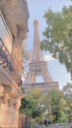 the eiffel tower in paris is seen through trees and people are walking on the sidewalk