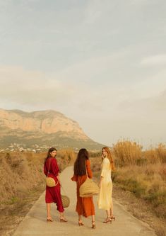 three women walking down a dirt road with mountains in the background