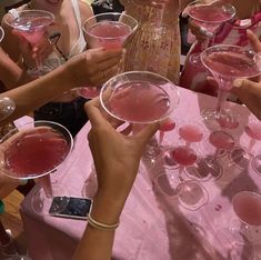 many people are holding up wine glasses with pink liquid in them and one person is holding a cell phone