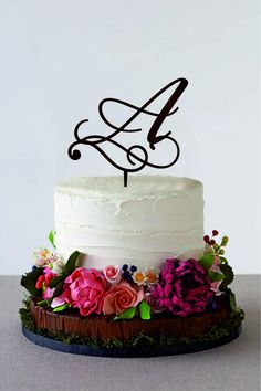 a white cake topped with a single letter and flowers