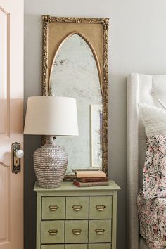 a bedroom with a dresser, mirror and lamp on top of the dresser is next to a bed