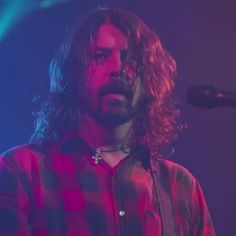 a man with long hair playing a guitar in front of a microphone at a concert