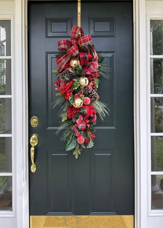 a christmas wreath on the front door of a house with pine cones and plaid ribbon