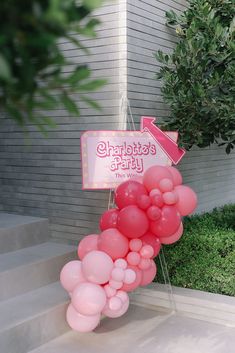 pink balloons are hanging from the side of a building with a sign that says charlotte's party