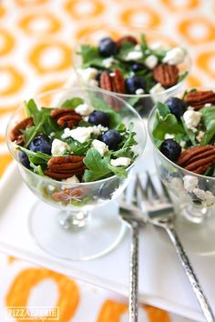 three clear bowls filled with salad and blueberries on top of a white table cloth