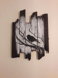 a piece of wood that has been painted with black and white paint on it, depicting a bird perched on a tree branch