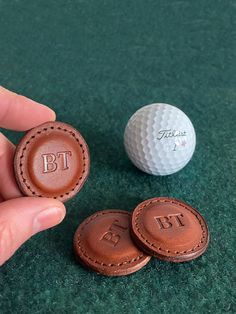 two golf balls sitting next to each other on a green carpeted area with a person's hand holding the ball