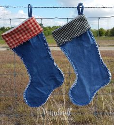 two christmas stockings hanging on a wire fence in the grass with a field behind them