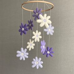 a mobile with purple and white flowers hanging from it's side on a gray background