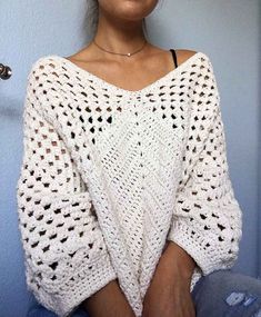 a woman wearing a white crochet sweater with her hands in her pockets and looking at the camera