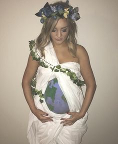 a woman in a white dress holding an earth globe on her stomach and wearing a flower crown