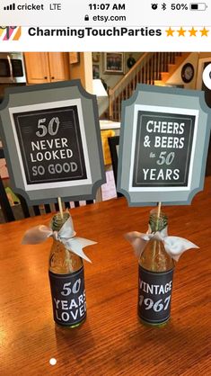 there are two beer bottles on the table with signs in them that say 50 years and cheers