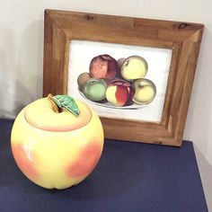 an apple sitting on top of a blue table next to a framed painting with apples in it