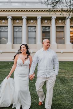 a bride and groom holding hands walking in front of a large white building with columns