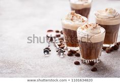 three cups filled with hot chocolate and whipped cream on top of coffee beans next to spoons