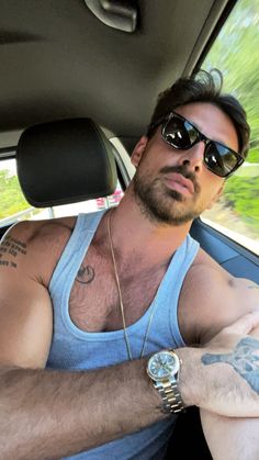 a man in sunglasses and a blue tank top is sitting in the back seat of a car