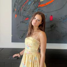 a girl in a yellow dress standing next to a painting