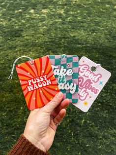 someone is holding three tags with words on them in front of a grassy field and green grass