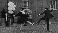 two people are dancing in front of a brick building with balloons and streamers on the ground