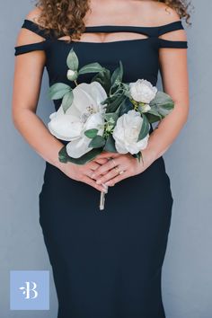 a woman in a black dress holding white flowers and greenery with her hands on her hips