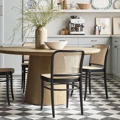 a kitchen table with chairs and plates on the wall above it, next to a potted plant