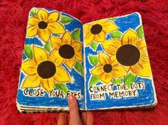 a hand holding an open book with sunflowers painted on it and the words close your eyes, connect the dots from memory