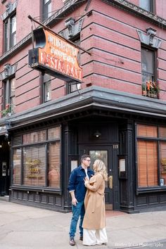 a man and woman standing in front of a restaurant with an orange sign on the building