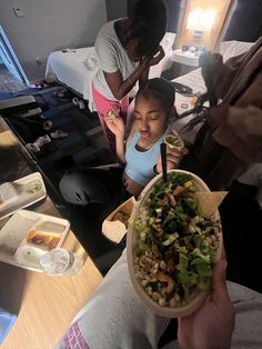 a person holding a bowl of food in front of two other people at a table