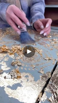 a person is painting on a metal surface with paintbrushes and gold flakes