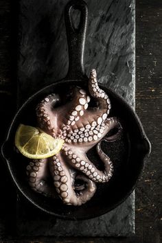 an octopus in a frying pan with a lemon slice on the side and black background