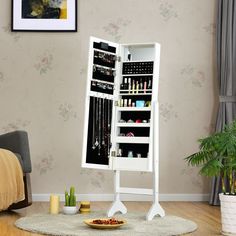 a white jewelry cabinet sitting on top of a wooden floor next to a chair and potted plant