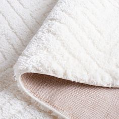 a close up view of a white blanket on a bed with a beige and white pillow