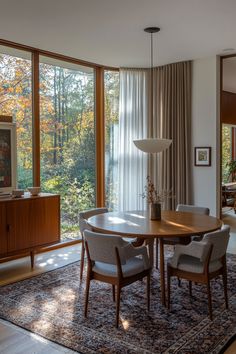 a dining room table with chairs and a rug on the floor in front of large windows