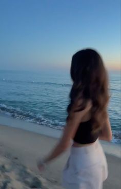 a woman is walking on the beach with her back to the camera and looking at the ocean