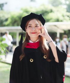 a young woman wearing a graduation gown and holding her hand up to her temple's ear