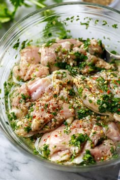 a glass bowl filled with meat covered in seasoning and garnished with herbs