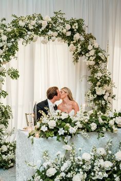 a bride and groom kissing in front of a floral arch