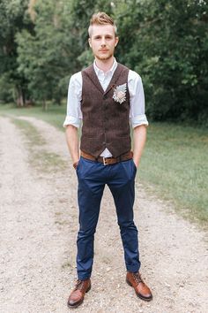 a man standing in the middle of a dirt road wearing a vest and bow tie