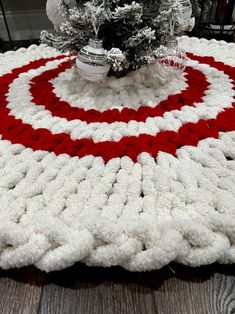 a red and white crocheted blanket sitting on top of a wooden floor next to a christmas tree