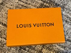 an orange box with the word louis vuitton written on it sitting on a carpet